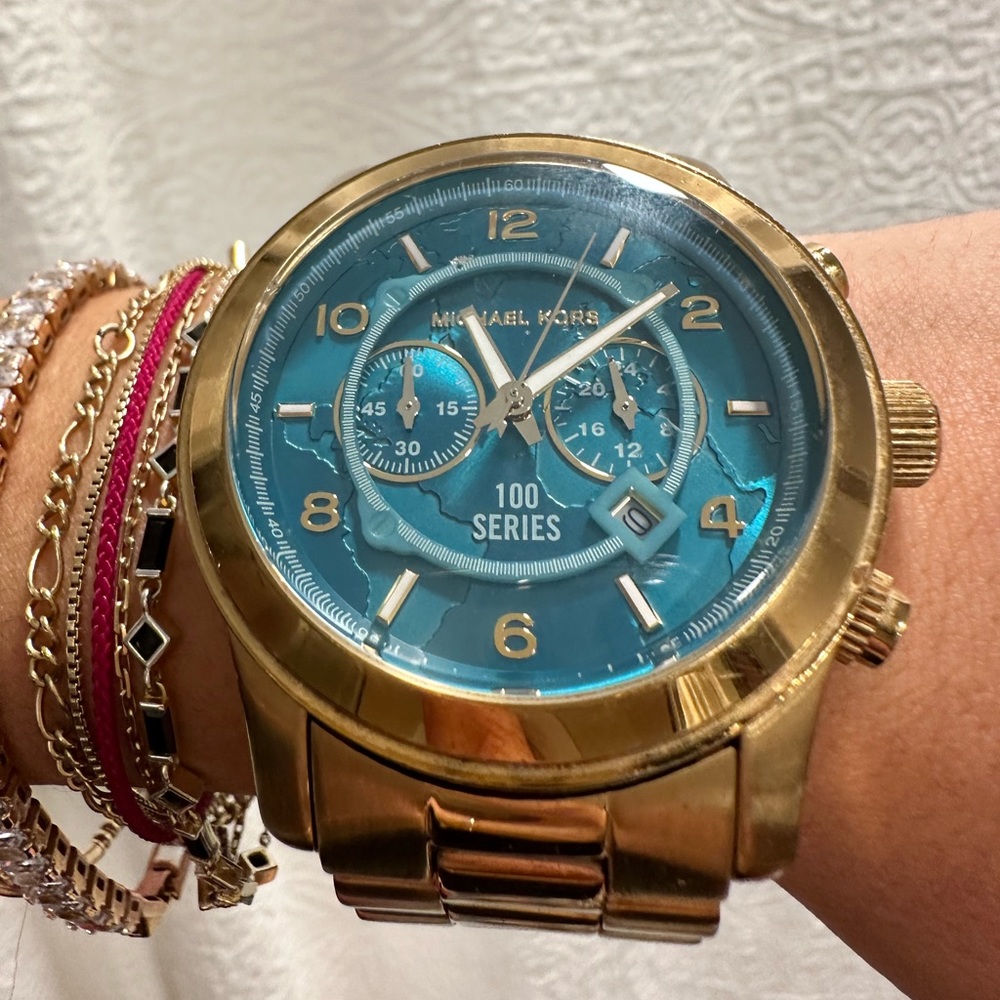 Michael Kors gold watch with oversized face.The face has an outline of the world